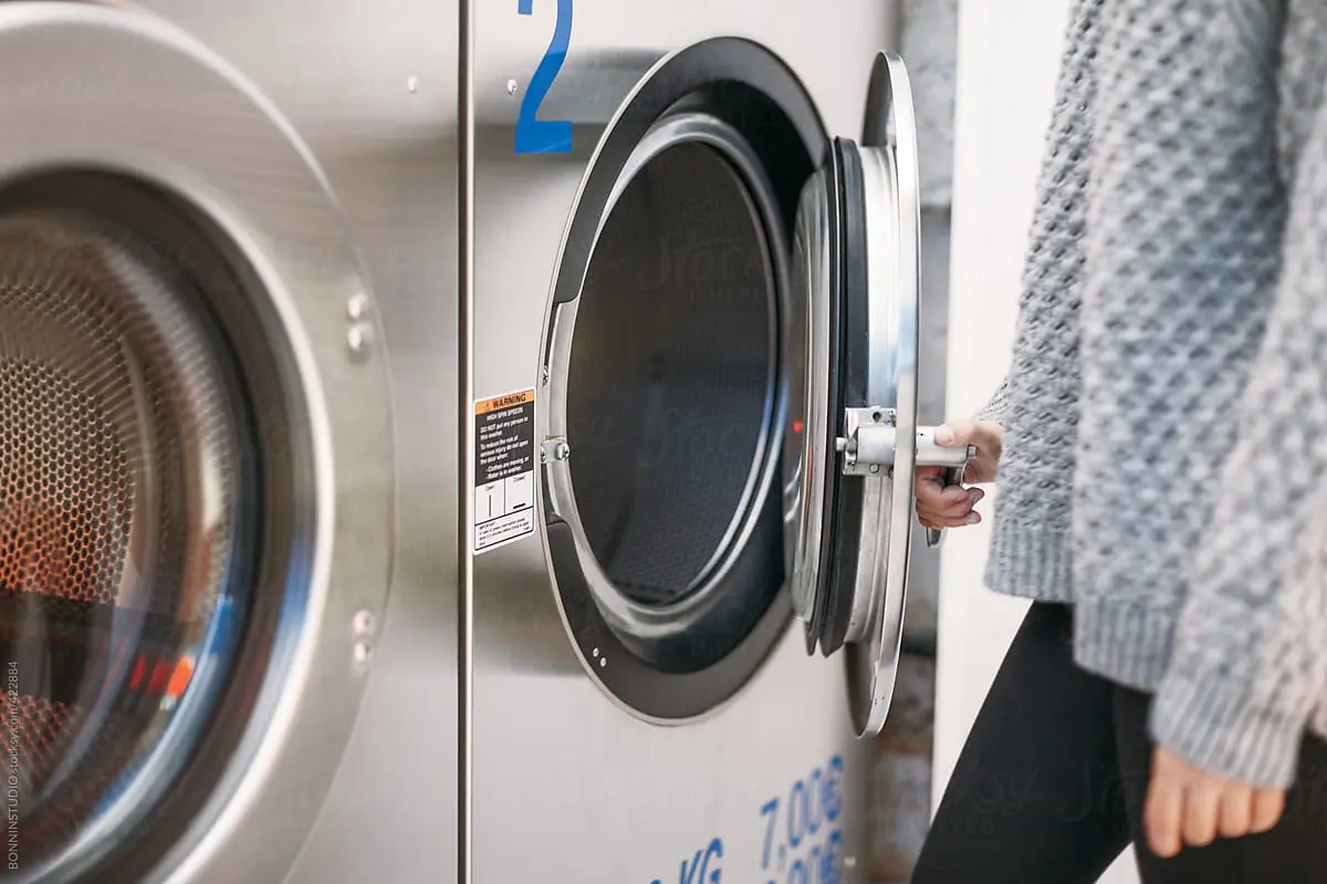 Hand opening the door of a commercial washing machine
